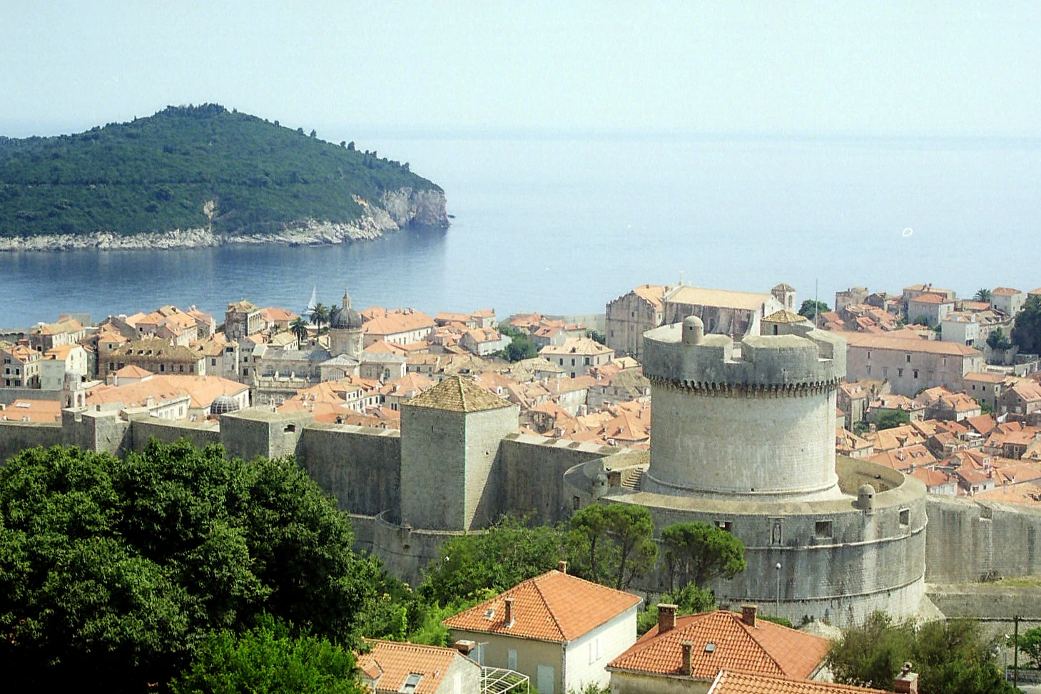 Nordwestlicher Abschnitt der Stadtmauer von Dubrovnik mit dem Rundturm Minčeta, roten Dächern der Altstadt und der Insel Lokrum im Hintergrund.