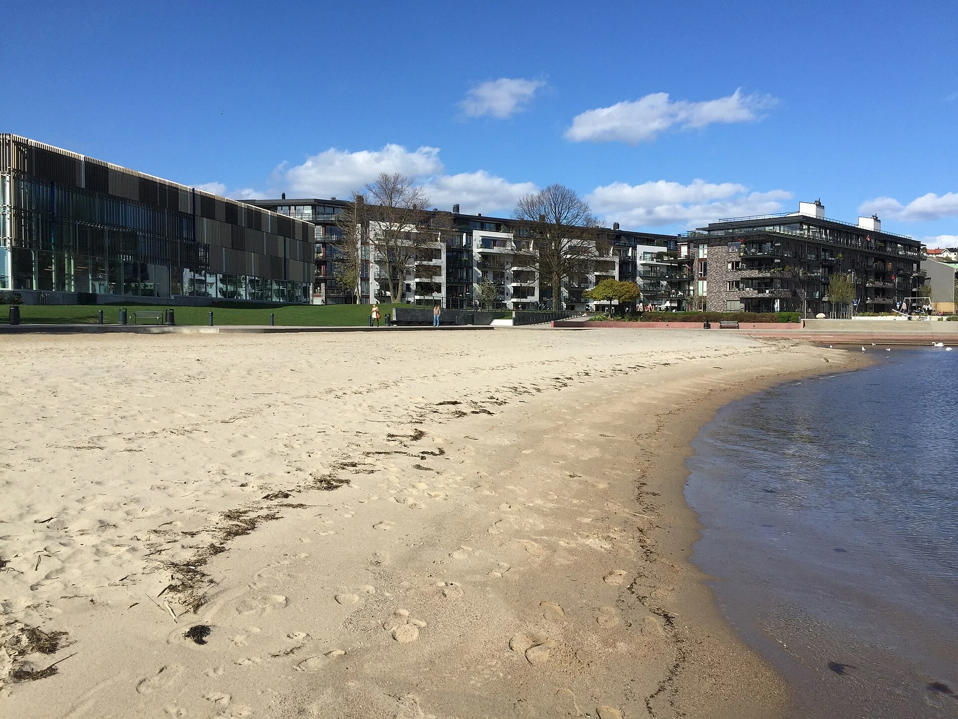 Bystranda in Kristiansand: geschwungener Sandstrand am Wasser, dahinter das Bad Aquarama und moderne Wohnhäuser.